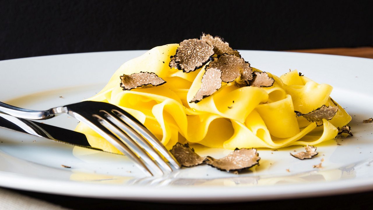 Breite Tagliatelle auf weißem Teller mit Trüffelscheiben und Gabel.