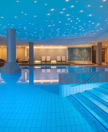 Innenpool im Wellnessbereich mit Sternenhimmel-Decke, Einstiegstreppe, Säulen und Ruheliegen.