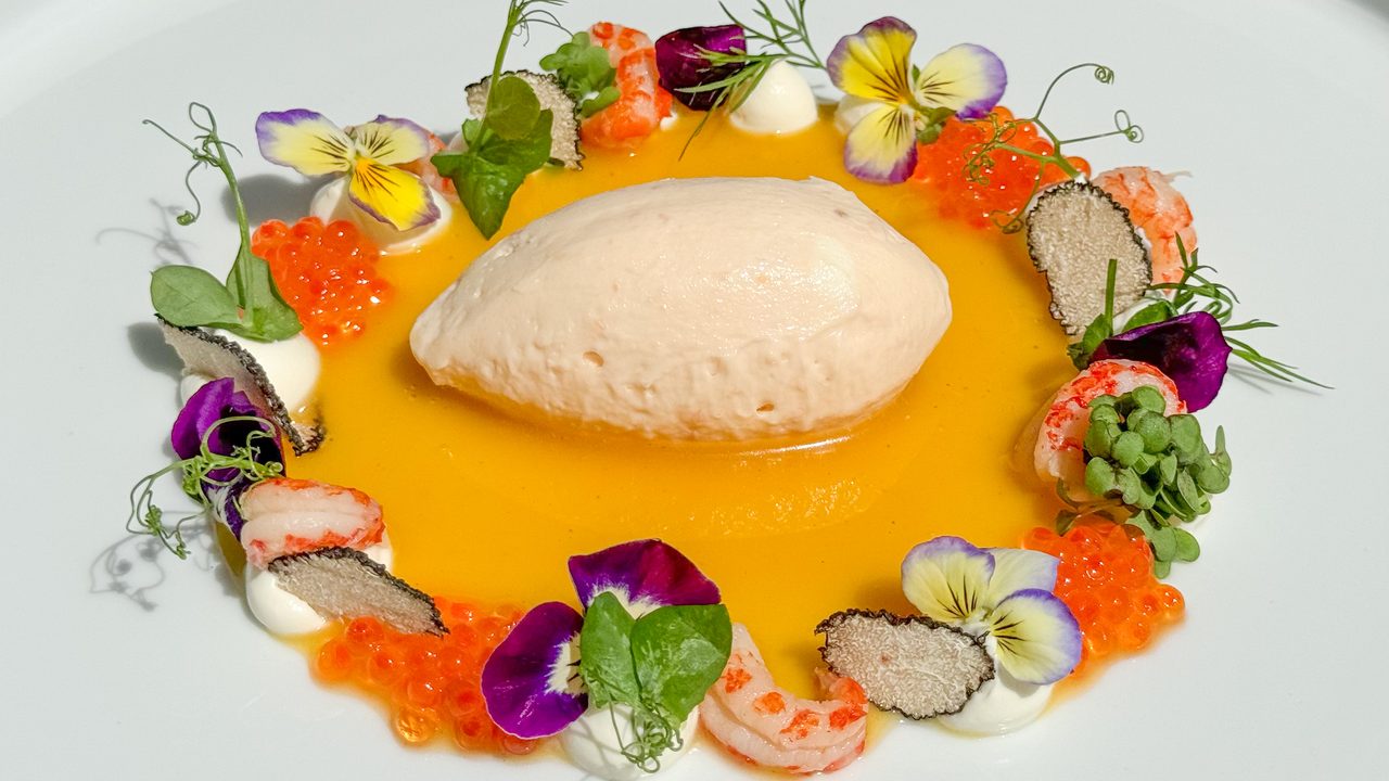 Kunstvoll angerichtete Vorspeise mit cremiger Nocke, gelber Sauce, Garnelen, Kaviar, Trüffelscheiben und Blüten.