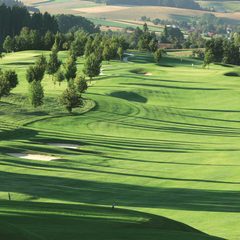 Golfplatz mit gepflegtem Fairway, Bäumen und Sandbunkern in hügeliger Landschaft.