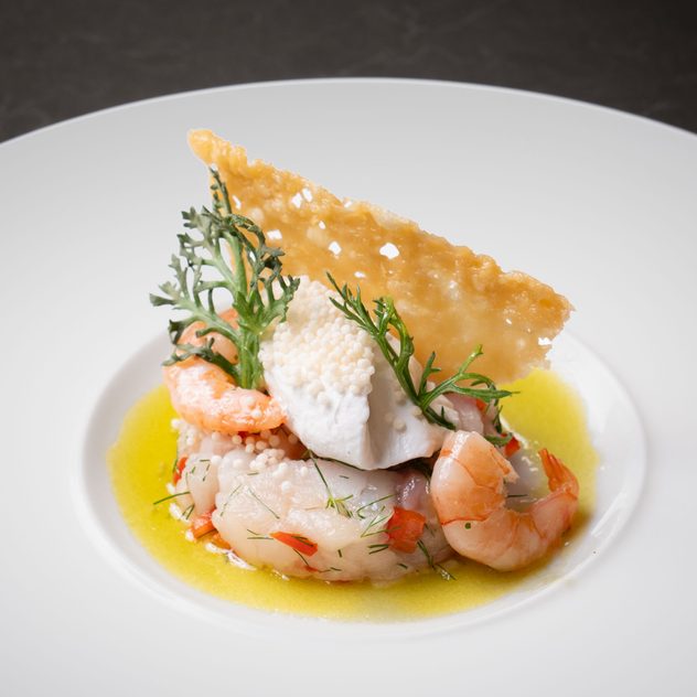 Vorspeise mit Garnelen, Fisch, Kräutern und gelber Sauce auf einem weißen Teller.