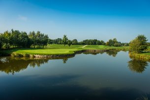 Golfplatz mit Putting Green an einem ruhigen See, umgeben von Bäumen und Wiesen.