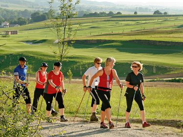 Eine Gruppe beim Nordic Walking auf einem Weg vor grüner Hügellandschaft und Golfplatz.
