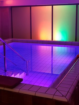 Kleiner Innenpool im Wellnessbereich mit Edelstahlgeländern und farbiger Beleuchtung an der Rückwand.