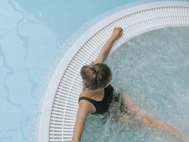 Frau im schwarzen Badeanzug entspannt in einem runden Whirlpool mit sprudelndem Wasser.