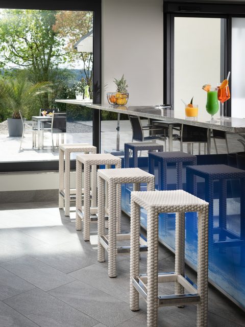 Moderne Hotelbar mit Barhockern, Cocktails auf dem Tresen und Blick durch große Fenster auf die Terrasse.