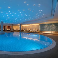 Großer Innenpool im Wellnessbereich mit beleuchteter Decke, Liegen und rundem Becken.