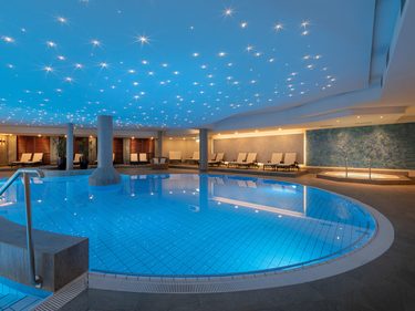 Großer Innenpool im Wellnessbereich mit beleuchteter Decke, Liegen und rundem Becken.