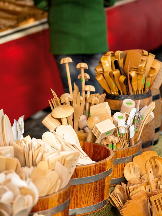 Verschiedene Küchenutensilien aus Holz stehen in Fässern an einem Marktstand im Außenbereich.