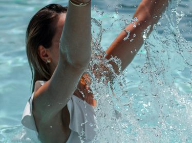 Eine Frau steht mit erhobenen Armen im Pool, während Wasser vor ihr hochspritzt.