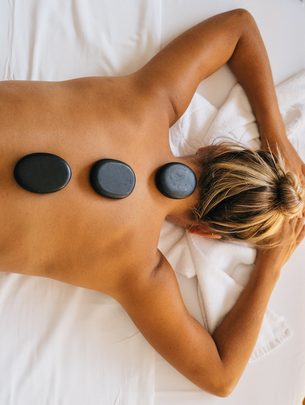 Frau liegt bei einer Hot-Stone-Massage auf einer Liege, vier schwarze Steine liegen auf ihrem Rücken.