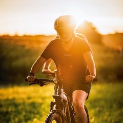 Person fährt mit einem Mountainbike über eine Wiese bei tief stehender Sonne.